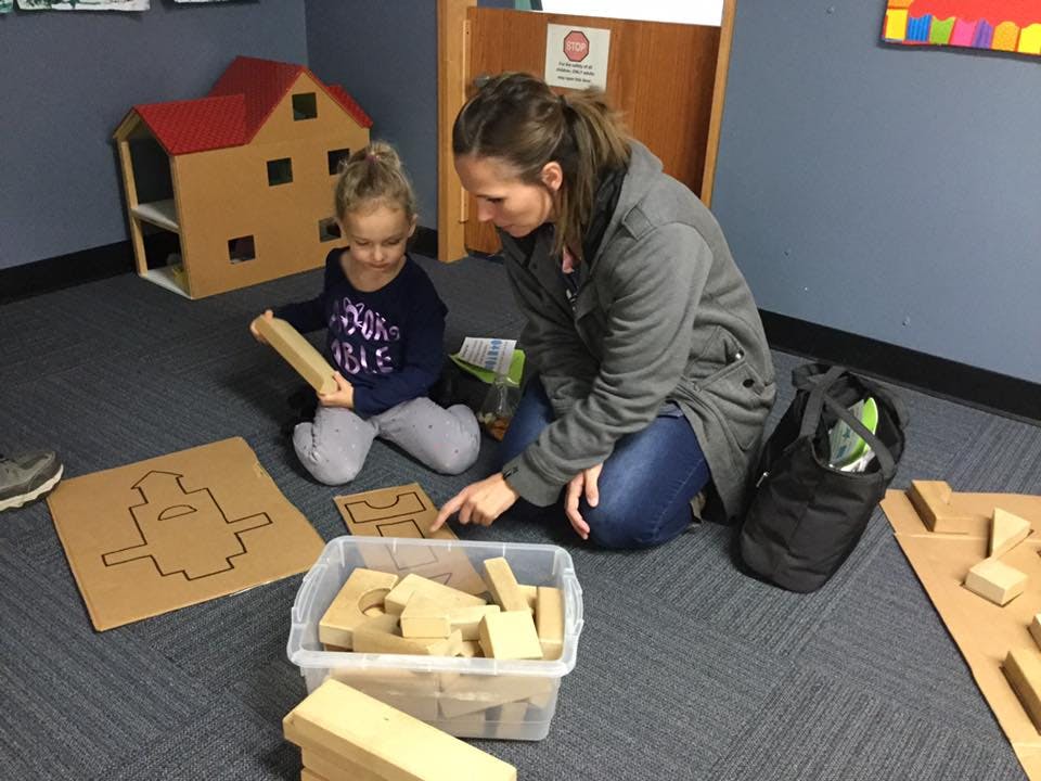 Adult and child kneeling on floor, playing with cardboard blocks