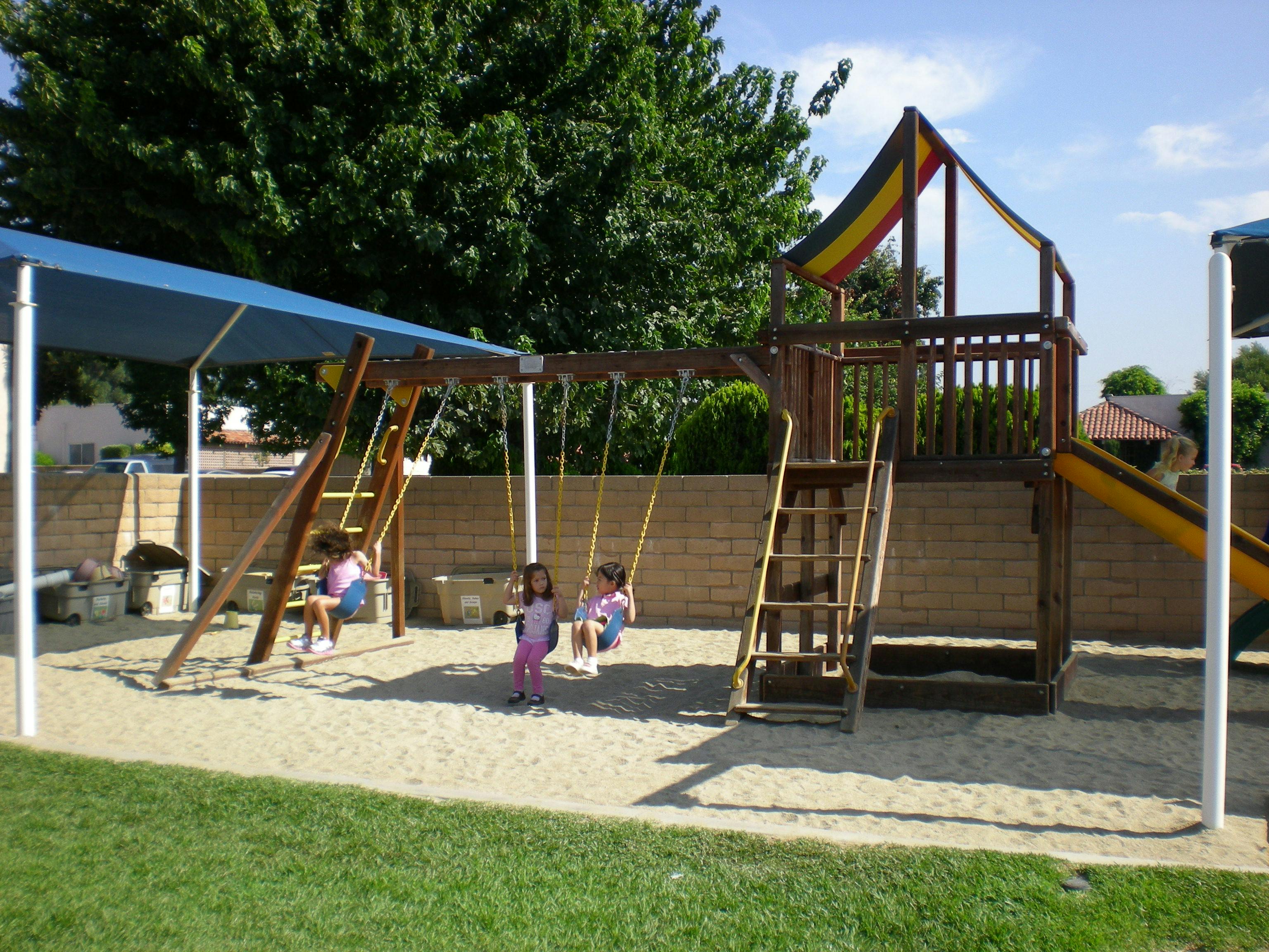 Children on swings and a play structure in a playground