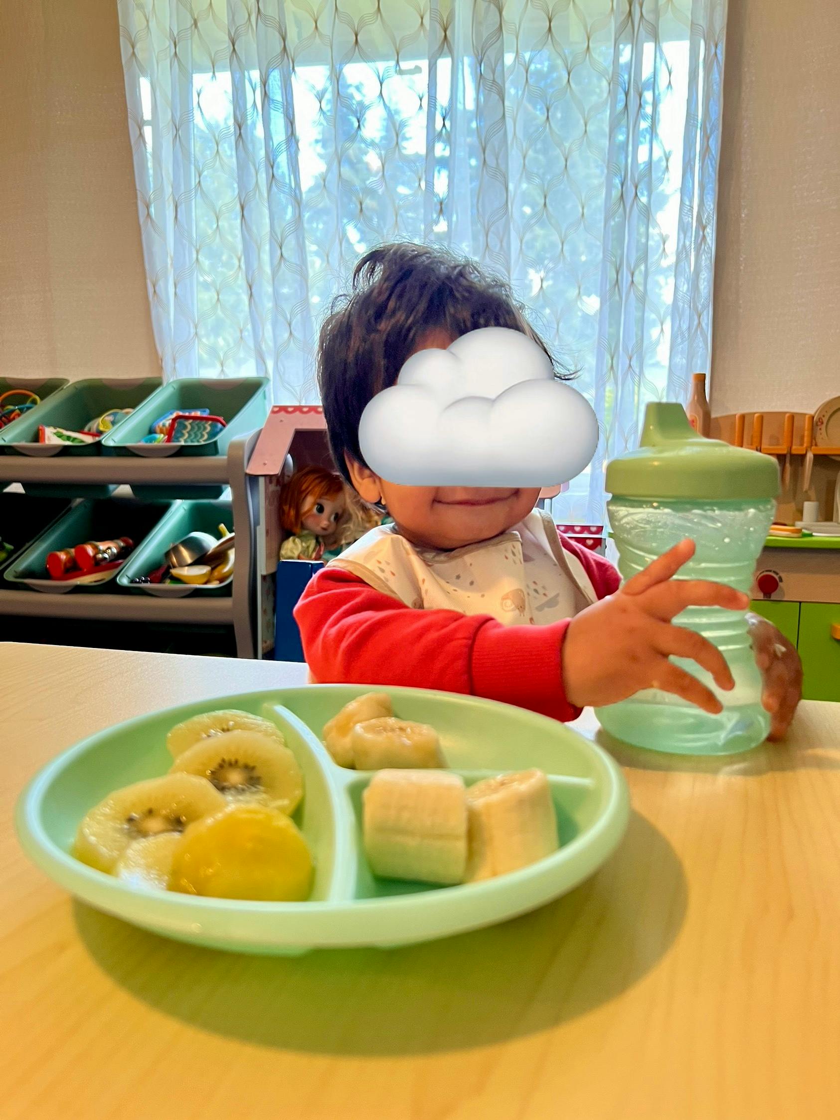 Child at a table with a plate of fruit and a sippy cup