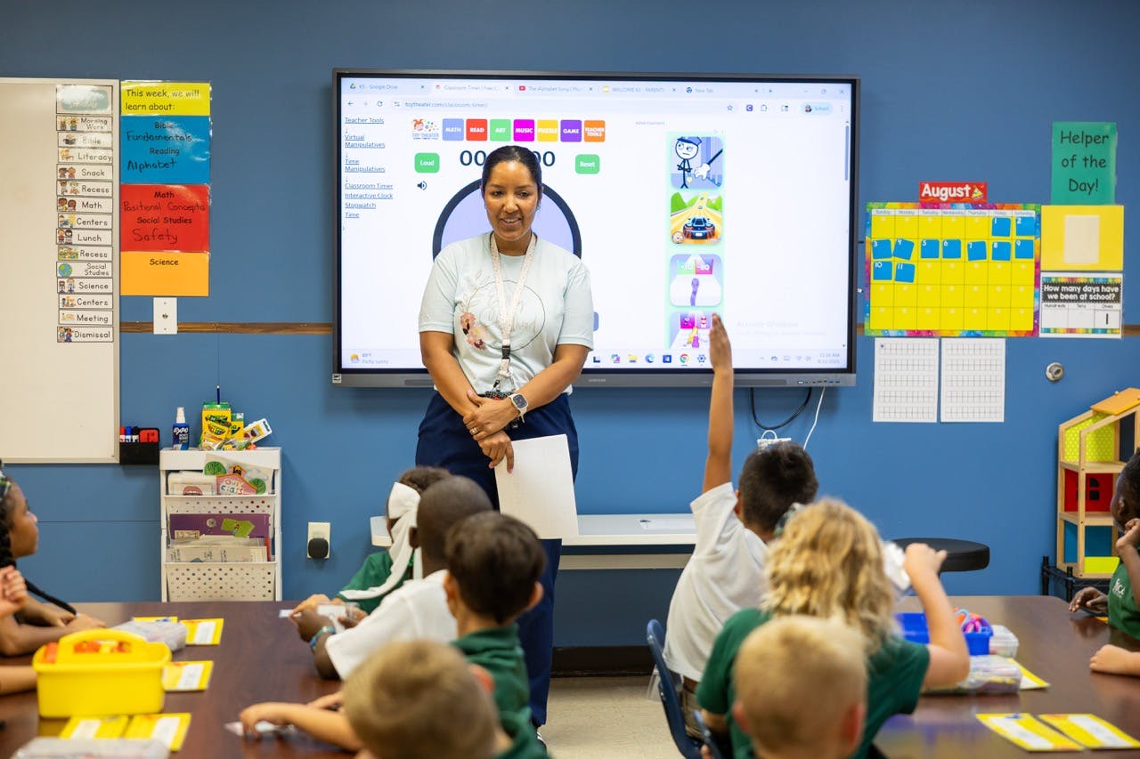 Person standing in front of a screen with children seated at desks