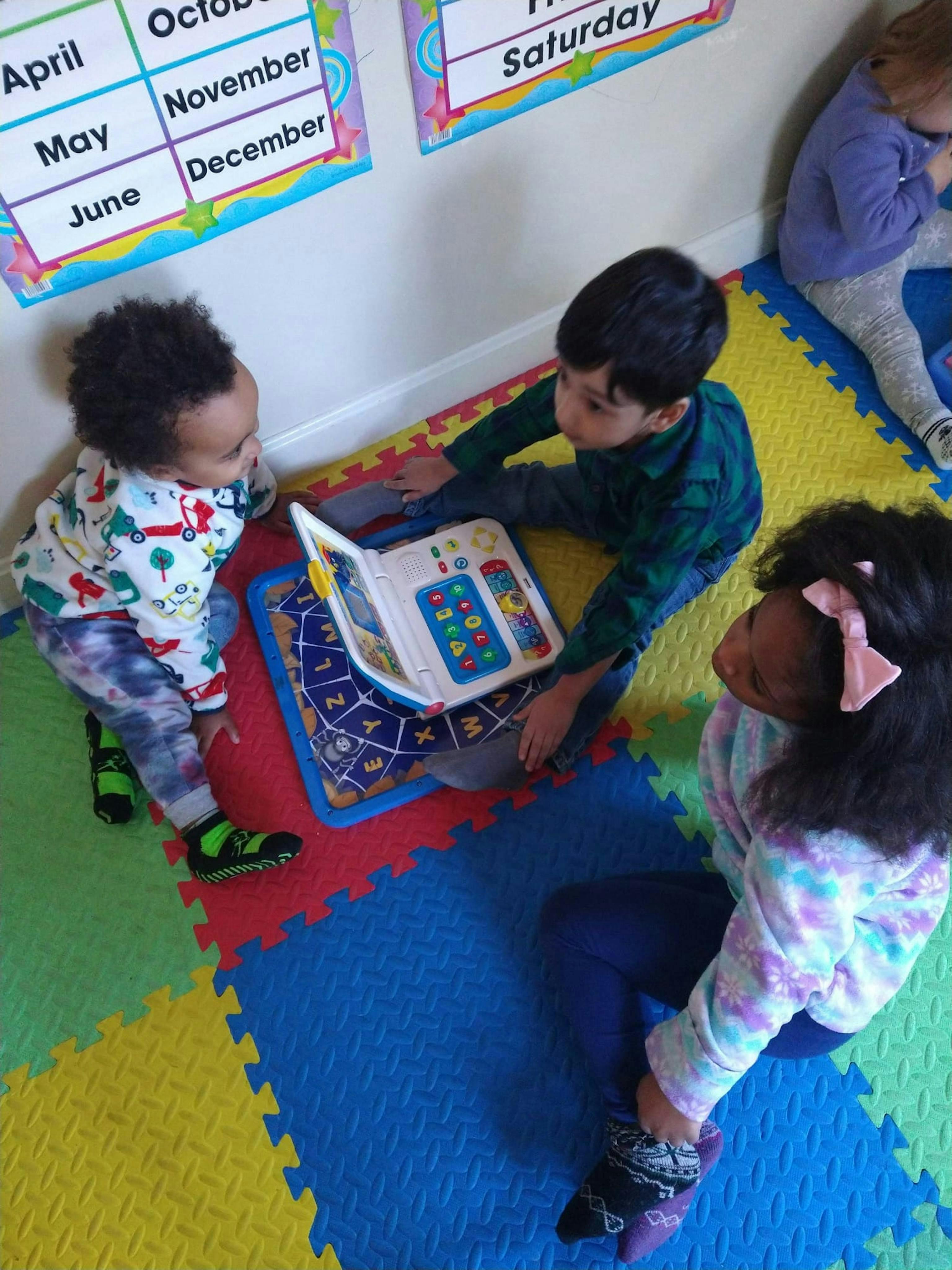Three children playing with an electronic book on a colorful mat