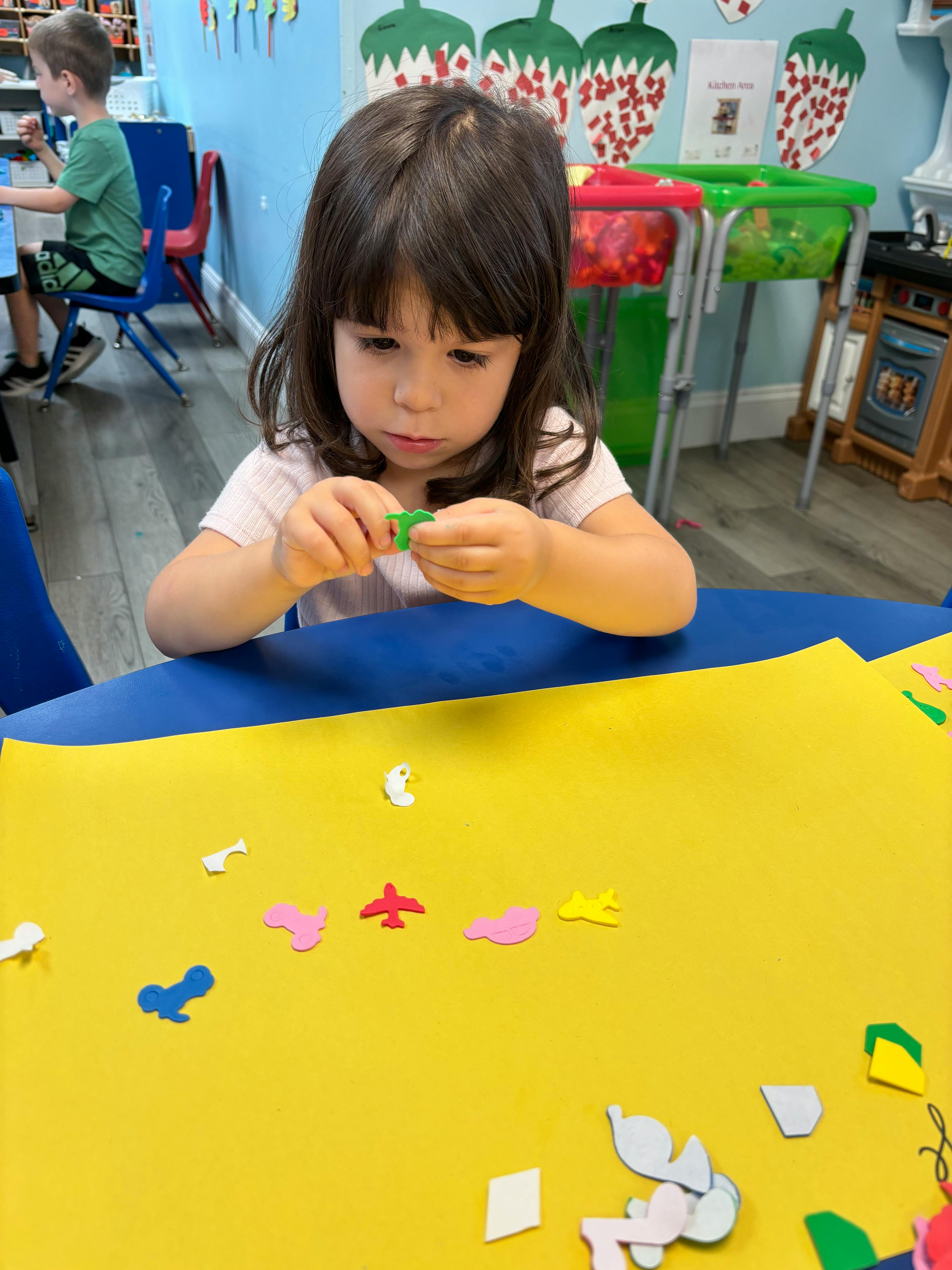 Child holding a small green shape over a yellow paper with cutouts