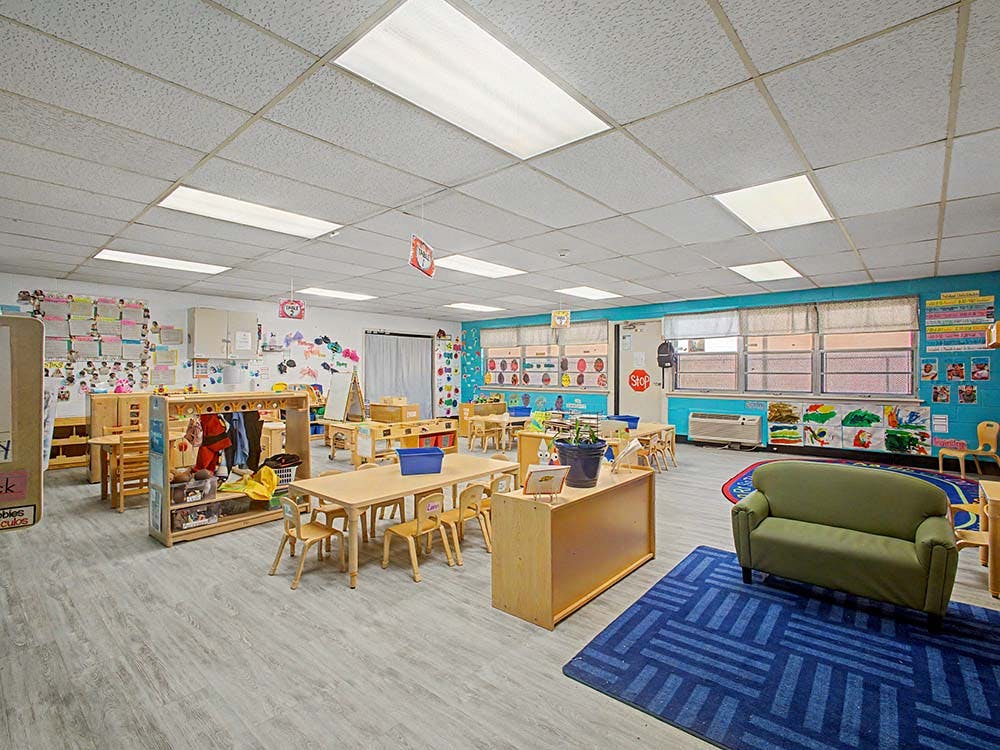 Classroom with small wooden tables and chairs, a green couch, and colorful decorations
