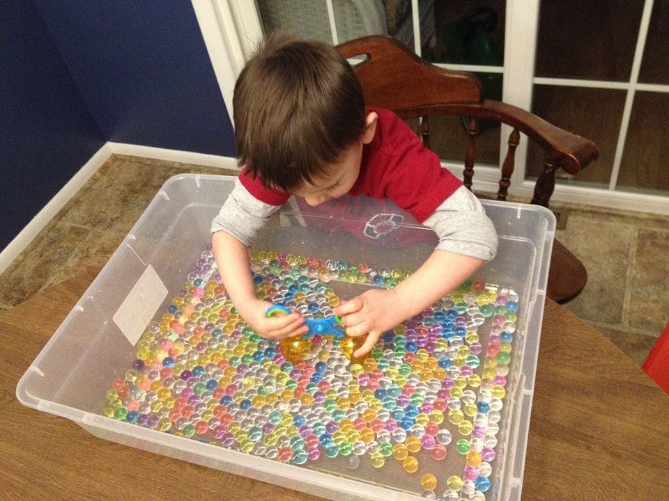 Child playing with colorful water beads in a clear bin