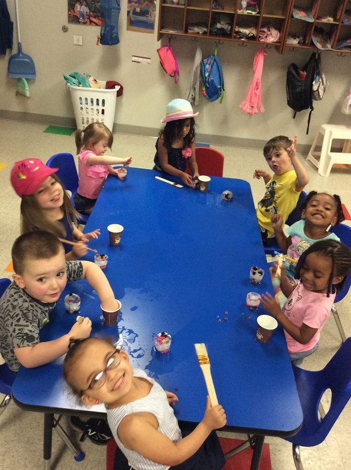 Children sitting around a blue table with cups and art supplies