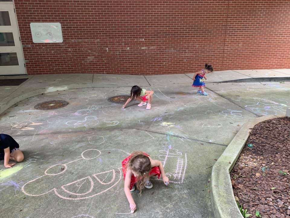 Three children drawing with chalk on pavement