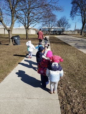 Children walking on a sidewalk with an adult in the distance