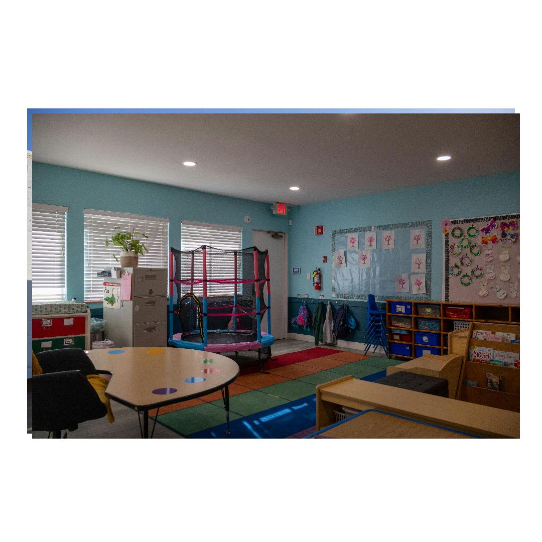 Empty preschool classroom with a small trampoline, tables, and play materials