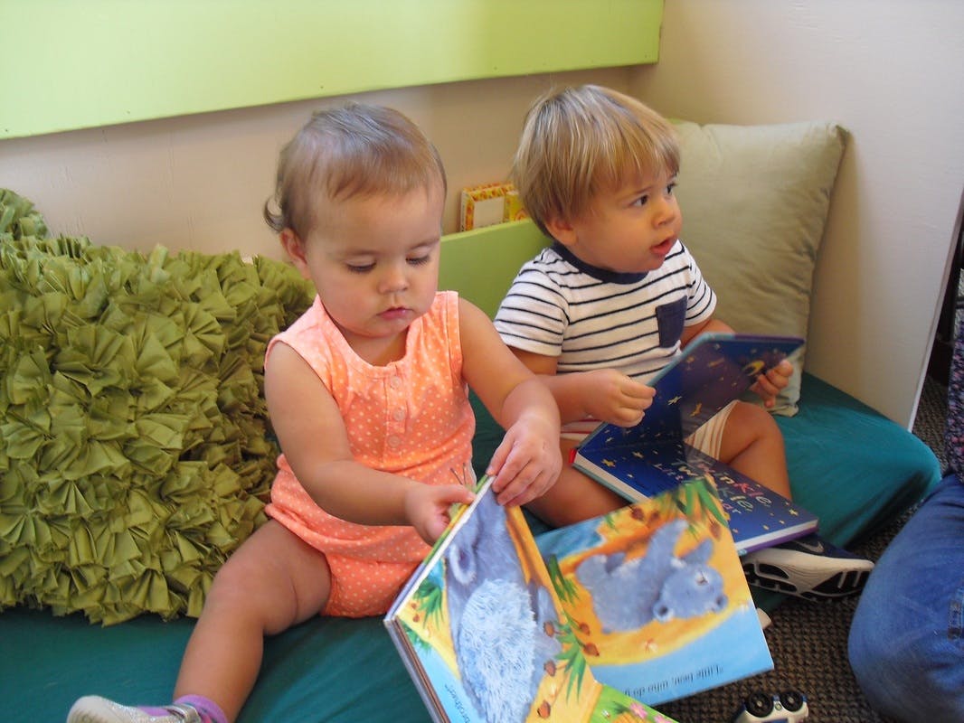 Two children sitting on a couch reading books