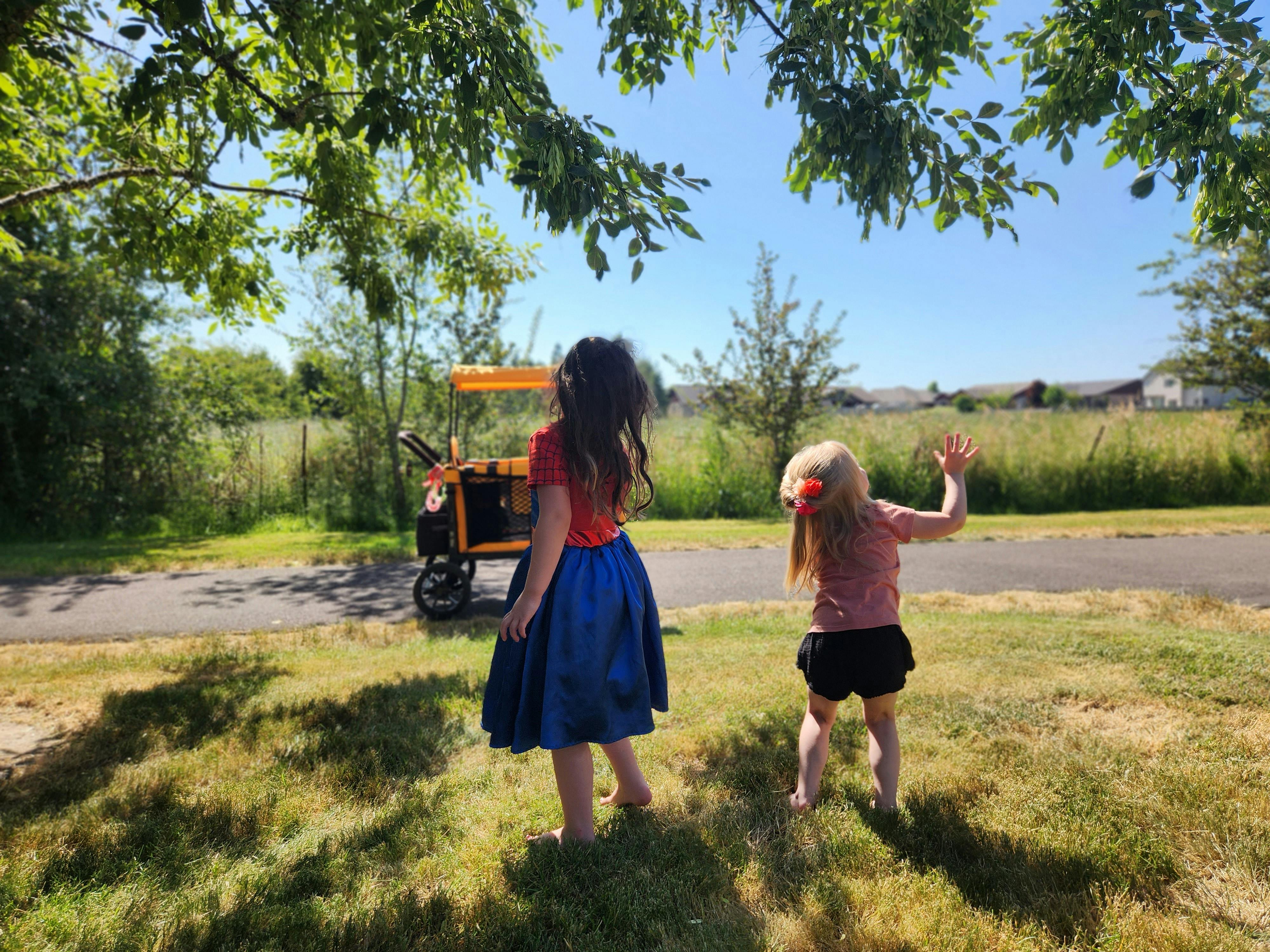 Two children standing on grass near a path with a cart