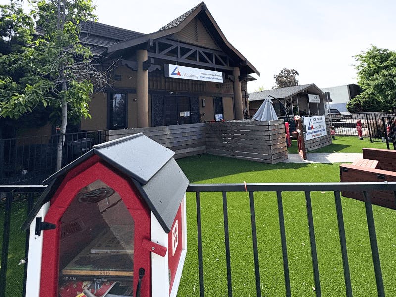 Red and white little free library in front of a building with green turf