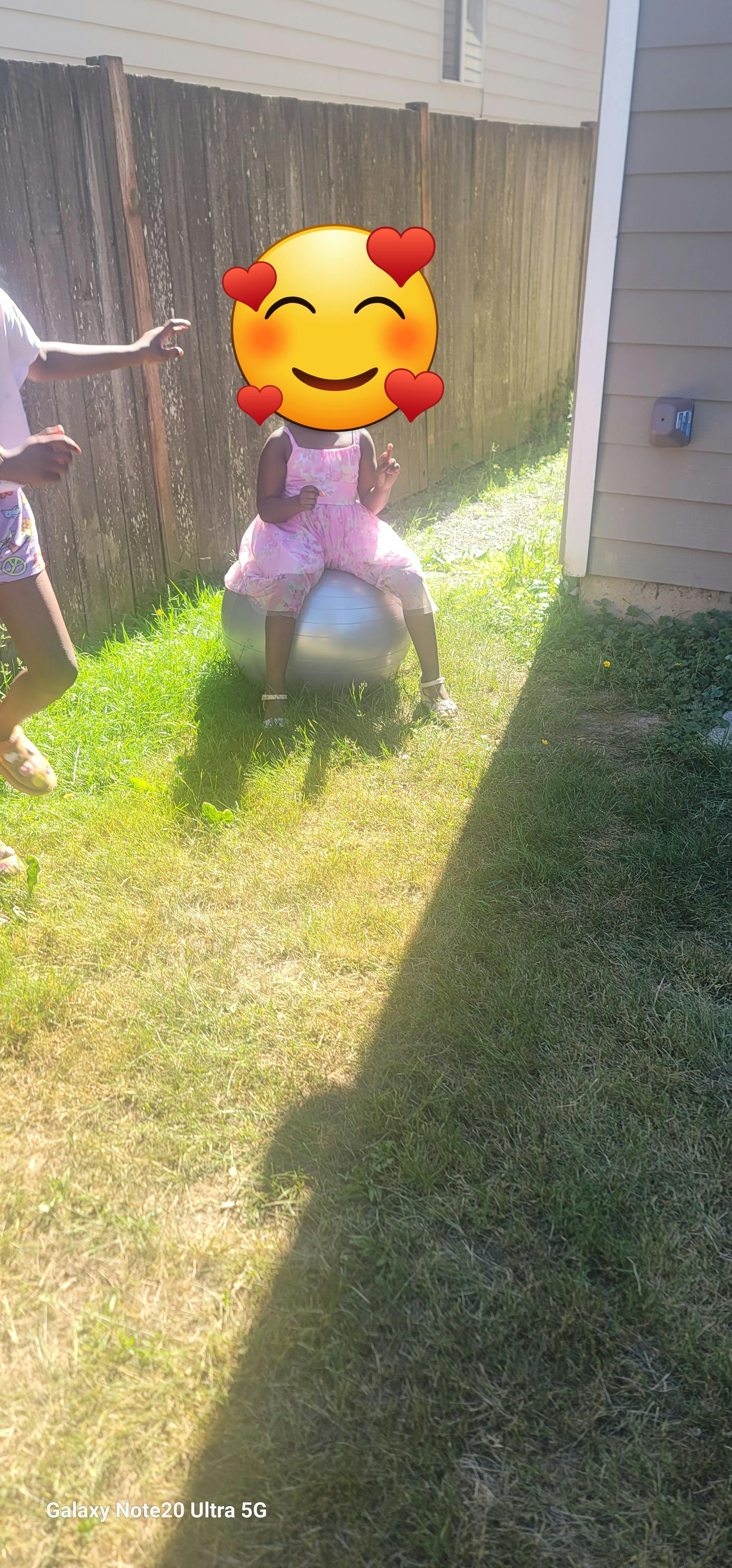 Child in a pink dress sitting on a large exercise ball outdoors