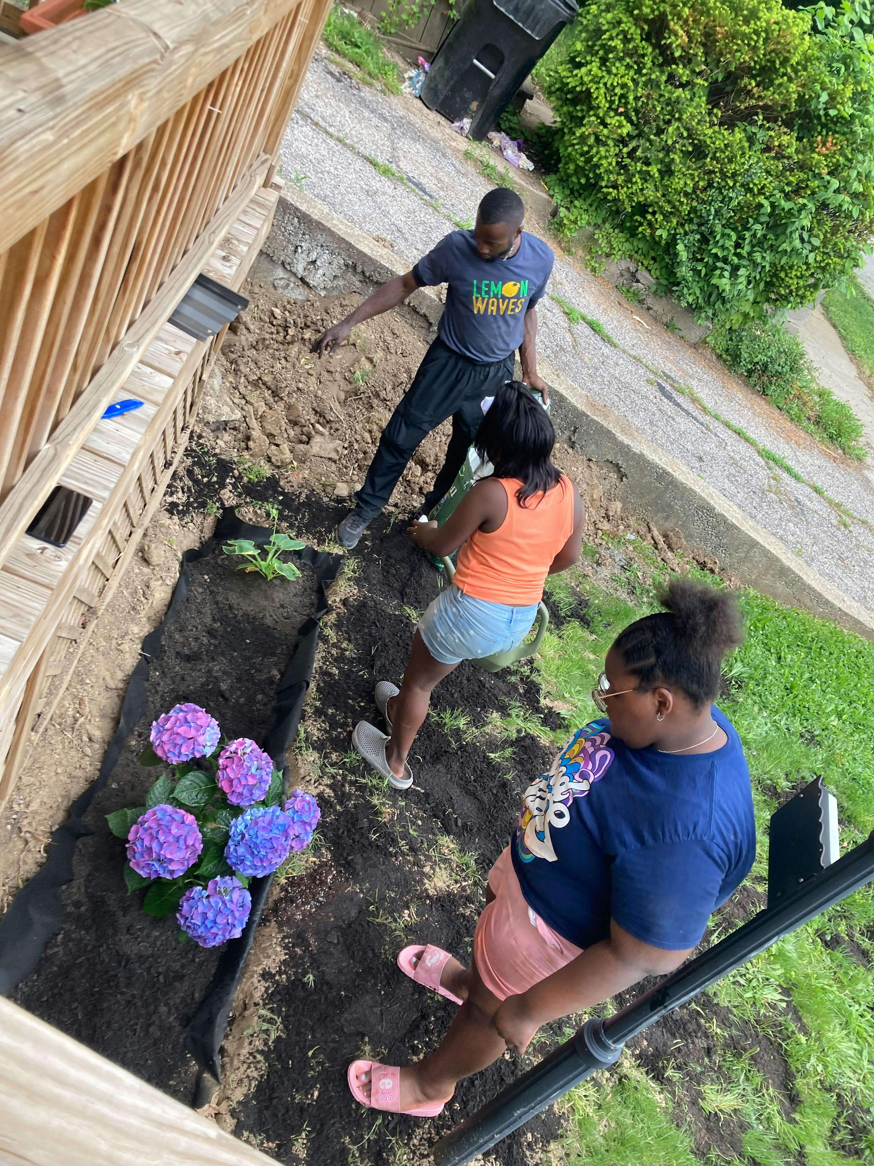 Three people planting in a garden bed with purple and blue flowers