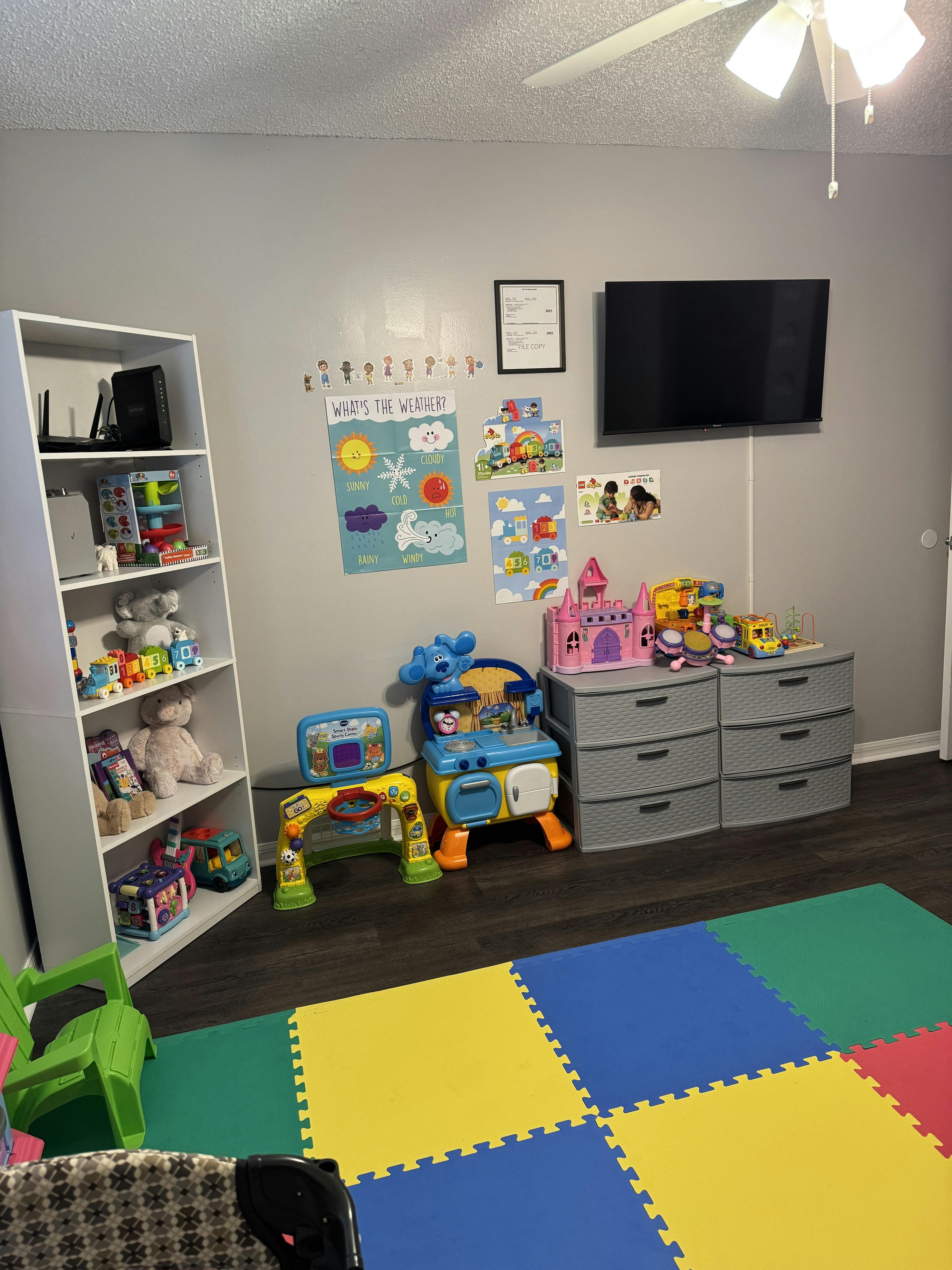 Playroom with colorful floor mats, toys, and a bookshelf