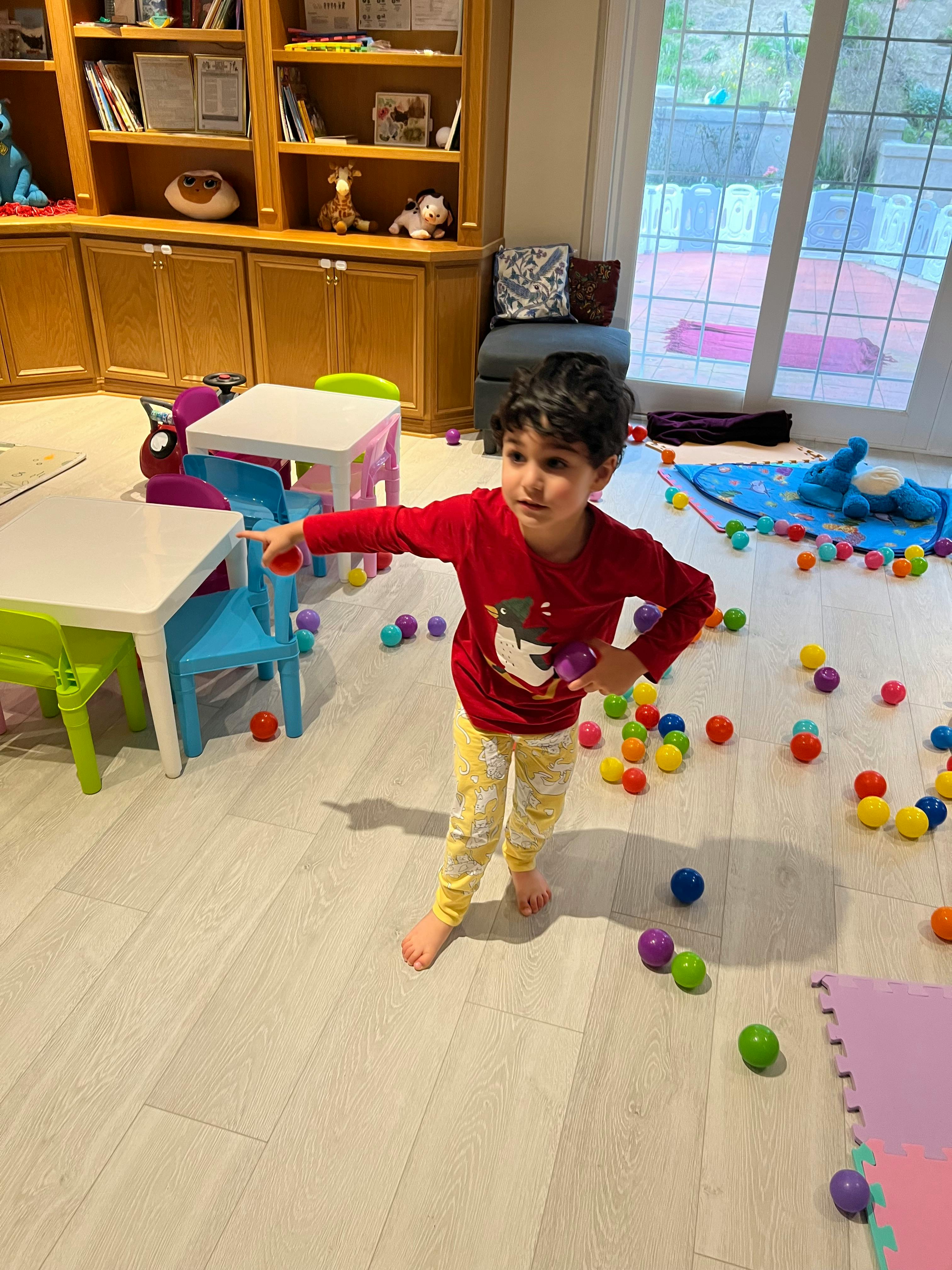 Child standing in a room with colorful balls on the floor, pointing