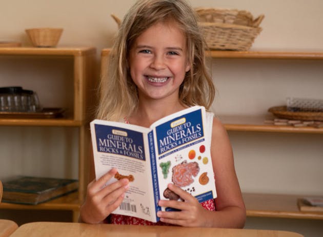 Child holding an open book titled "Guide to Minerals, Rocks & Fossils"