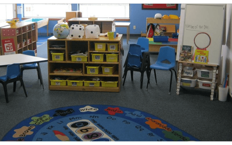 Classroom with children's furniture, shelves with yellow bins, and a whiteboard