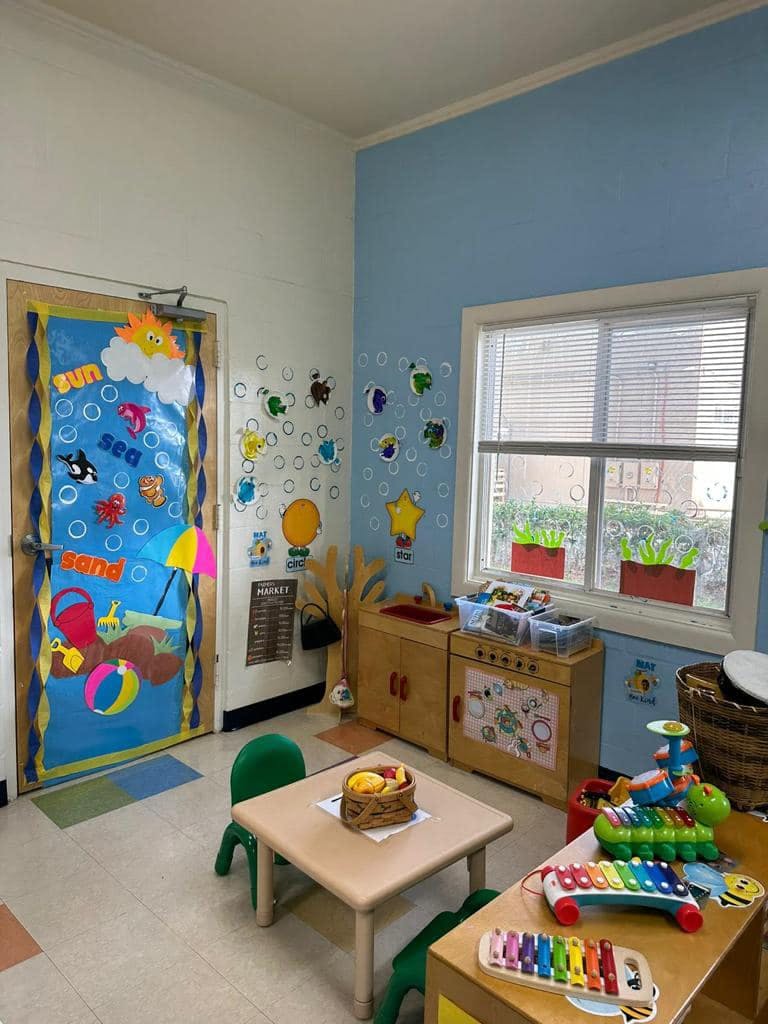 A classroom with a decorated door, small tables and chairs, and play kitchen