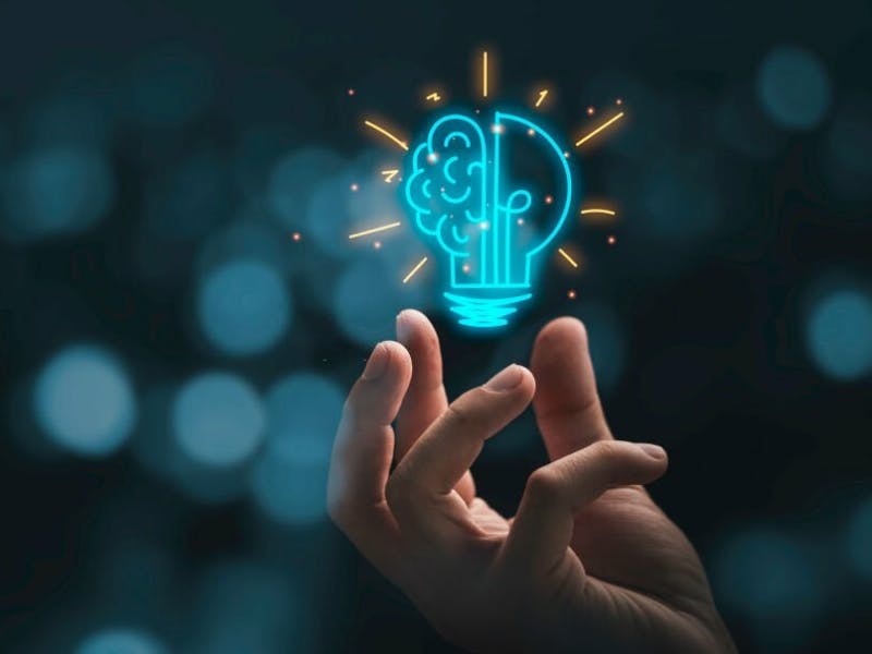Hand holding a glowing lightbulb illustration with a brain inside