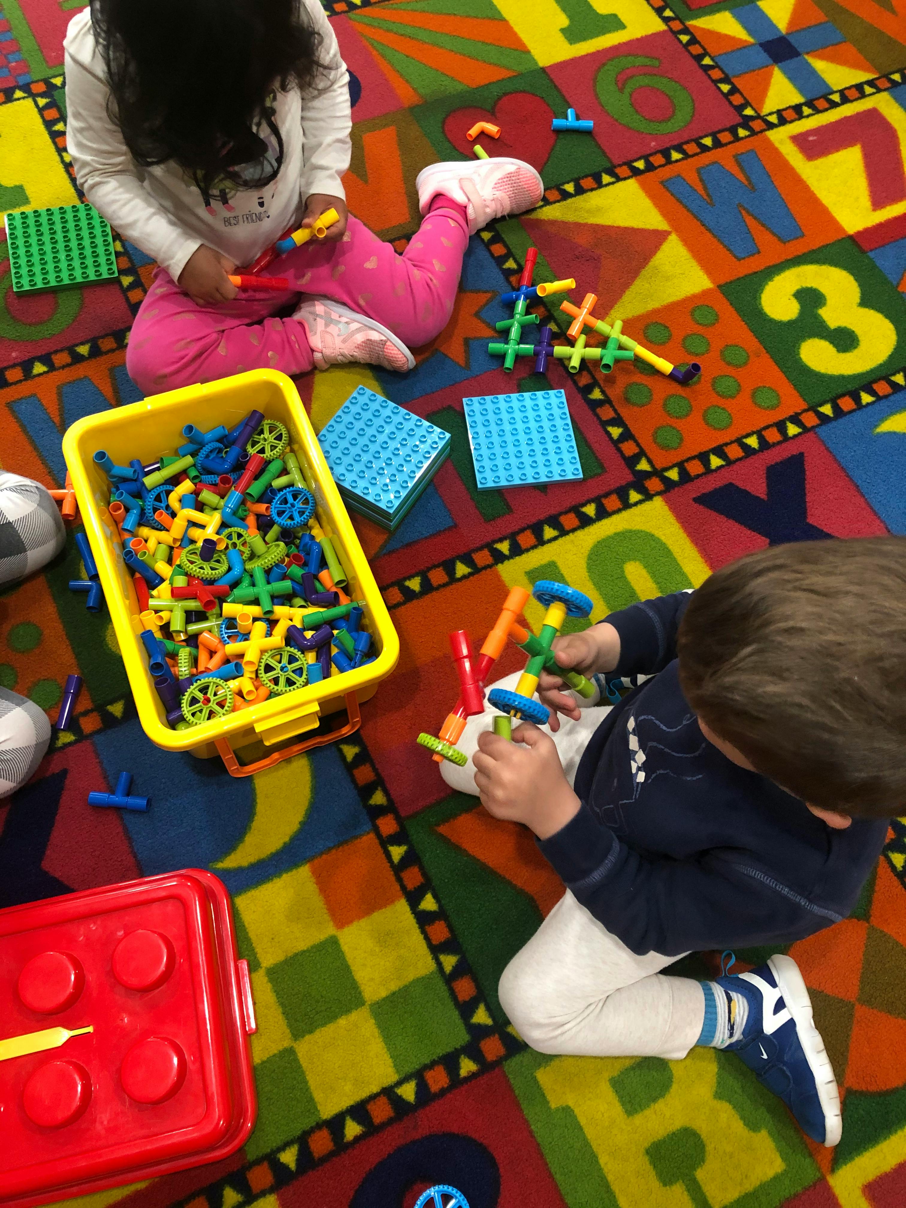 Two children playing with building toys on a colorful rug
