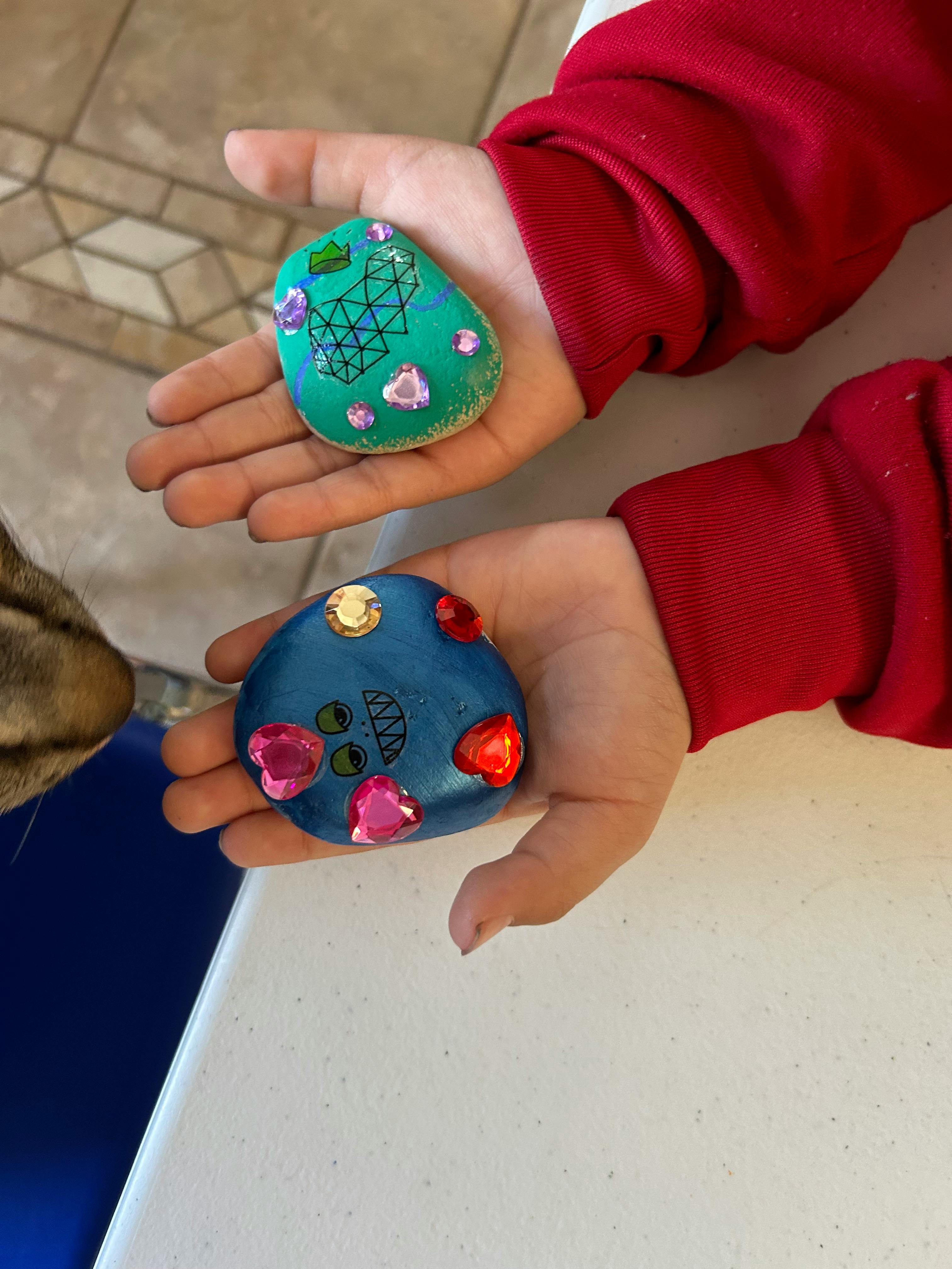 Person holding two decorated rocks with gems