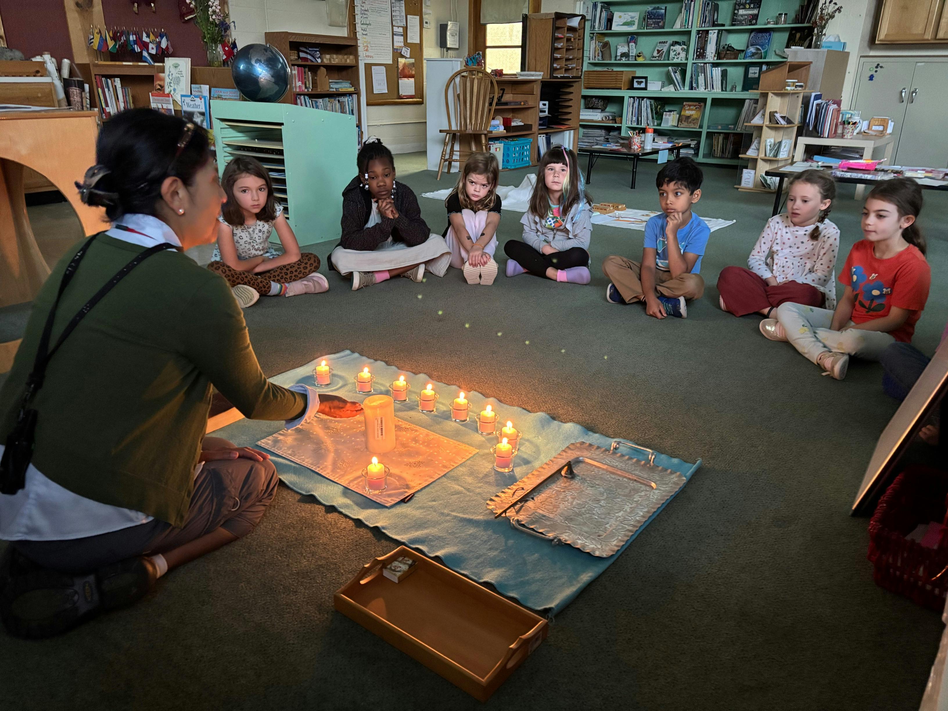 Person and children sitting in a circle around lit candles