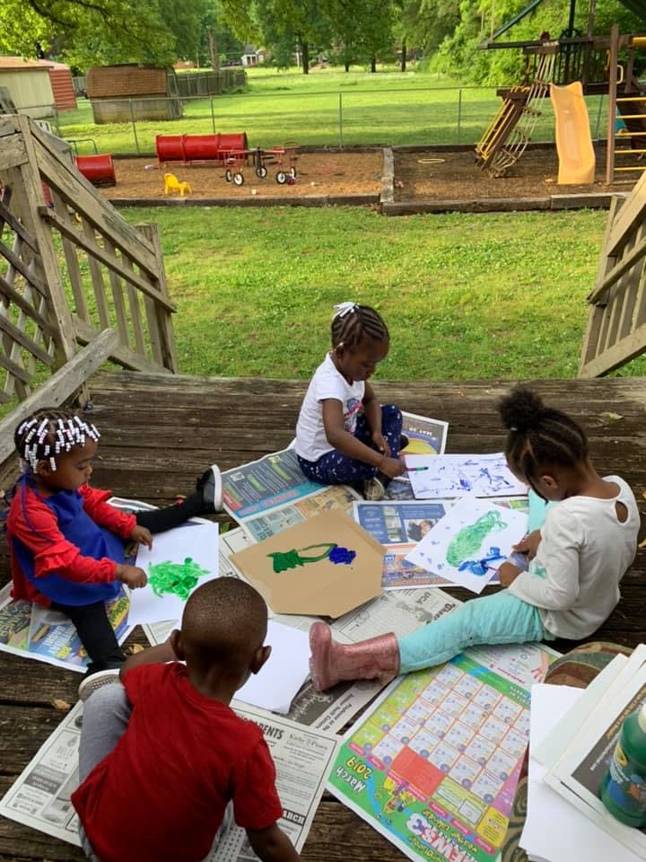Three children painting and drawing on a wooden deck