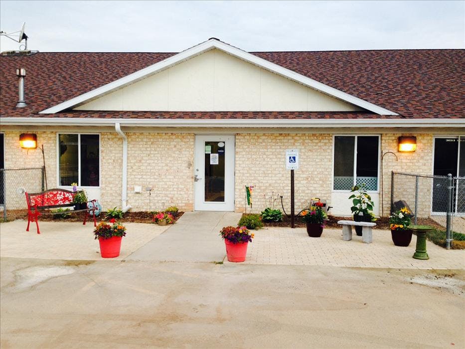 Entrance of a building with light brick, a brown roof, and flowers in planters