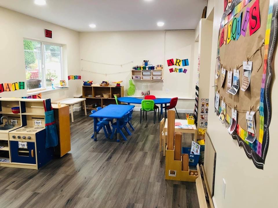 Classroom with blue tables and chairs, play kitchen, and wall decorations