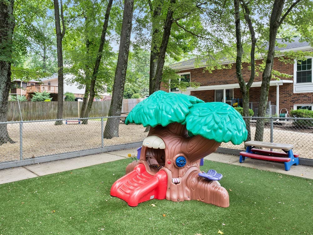A treehouse-shaped play structure with a red slide on artificial grass