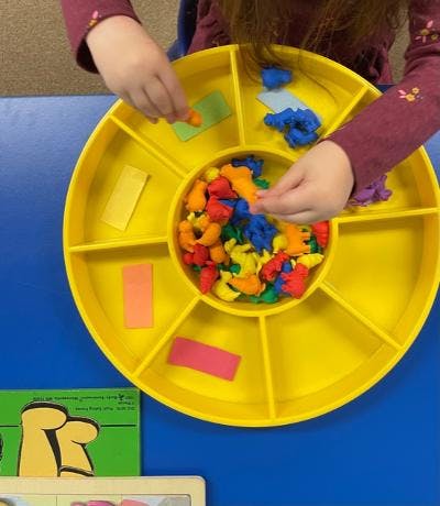 Child sorting colorful small objects into a yellow tray