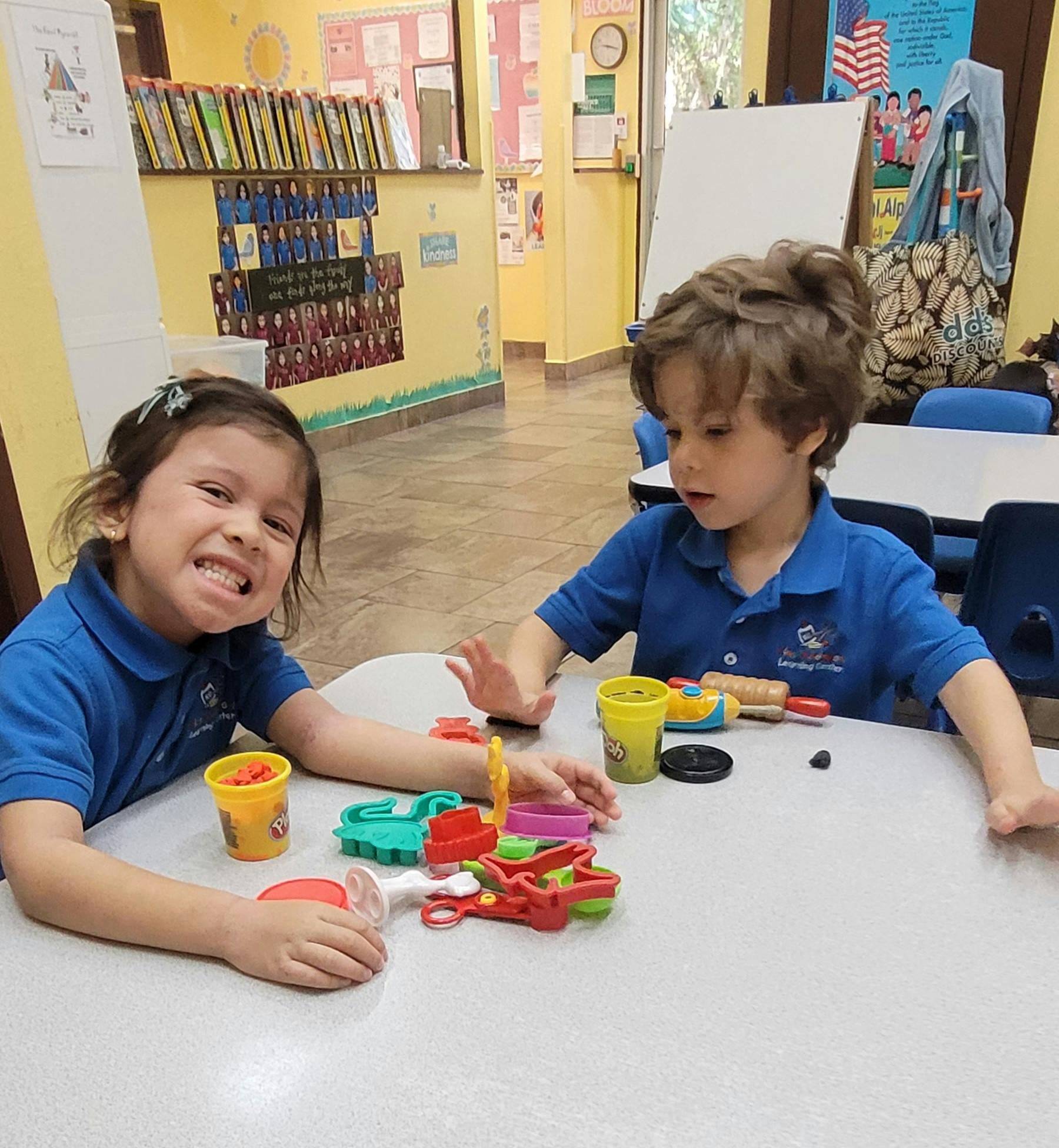Two children playing with modeling clay at a table in a classroom