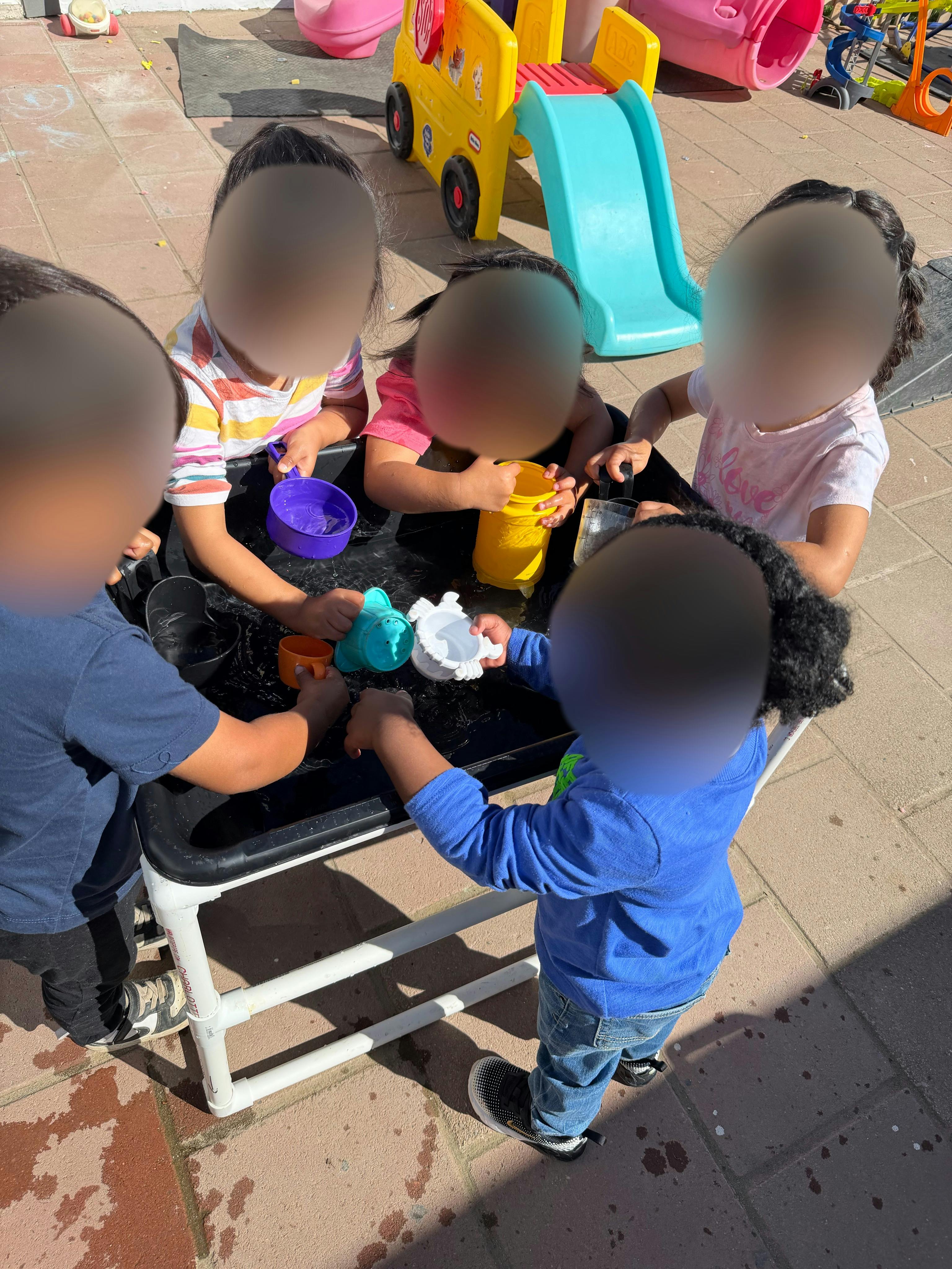 Several children playing around a black water table with colorful cups and toys