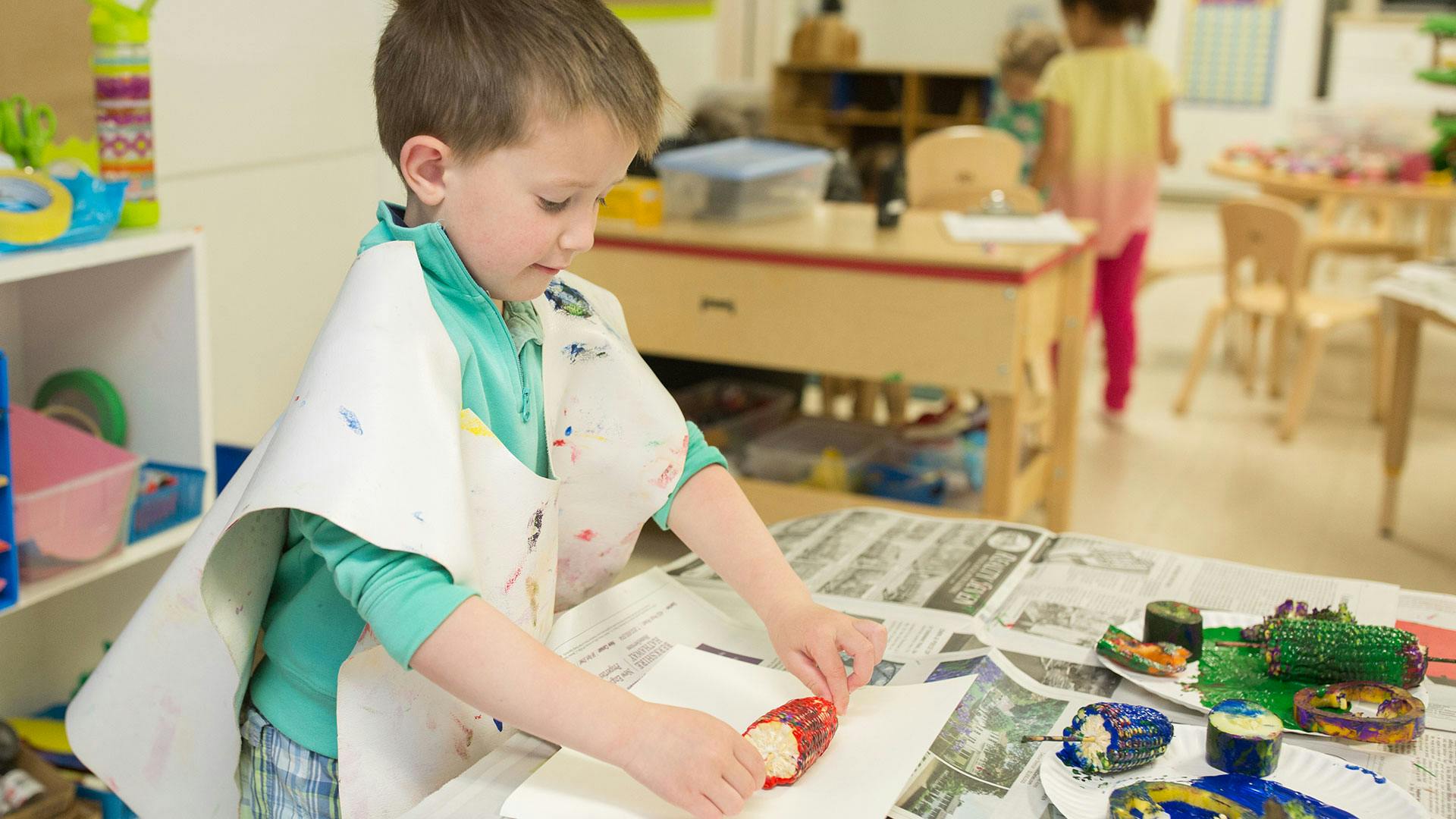 Child in an apron working on a craft project at a table