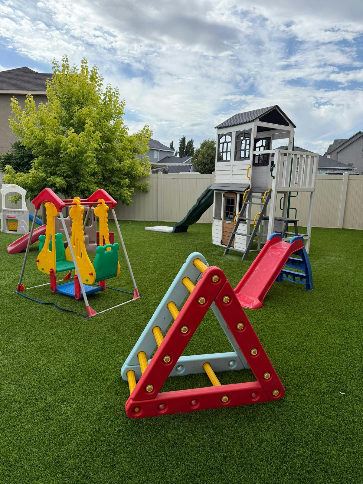 Outdoor playground with swings, slides, and a playhouse on artificial turf