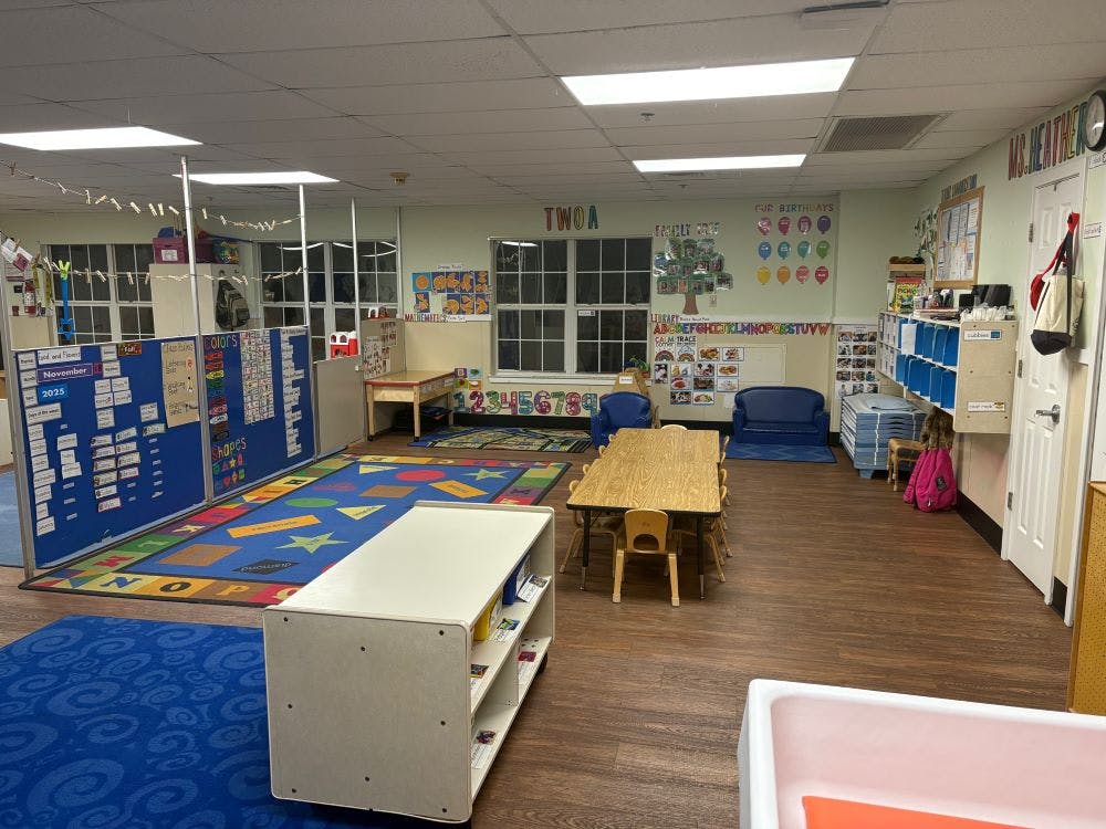 Empty classroom with colorful rugs, small tables, and learning displays