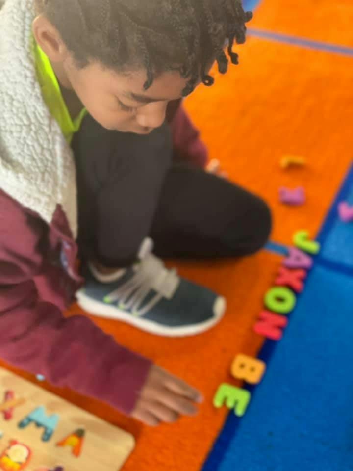 Child on floor playing with letter magnets spelling "JAXON BE"