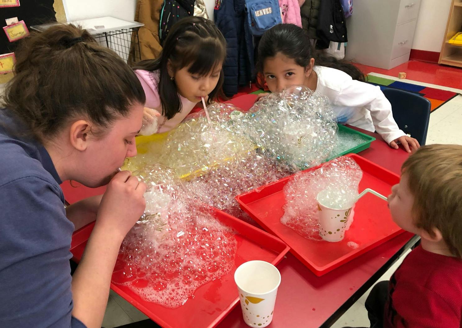 Person and children blowing bubbles with straws into trays