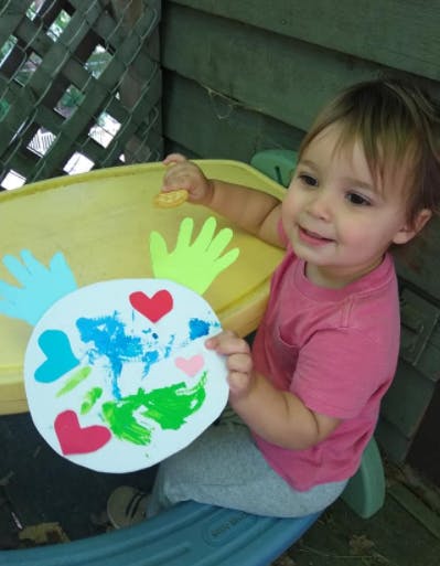 Child holding a paper plate with painted hearts and handprints