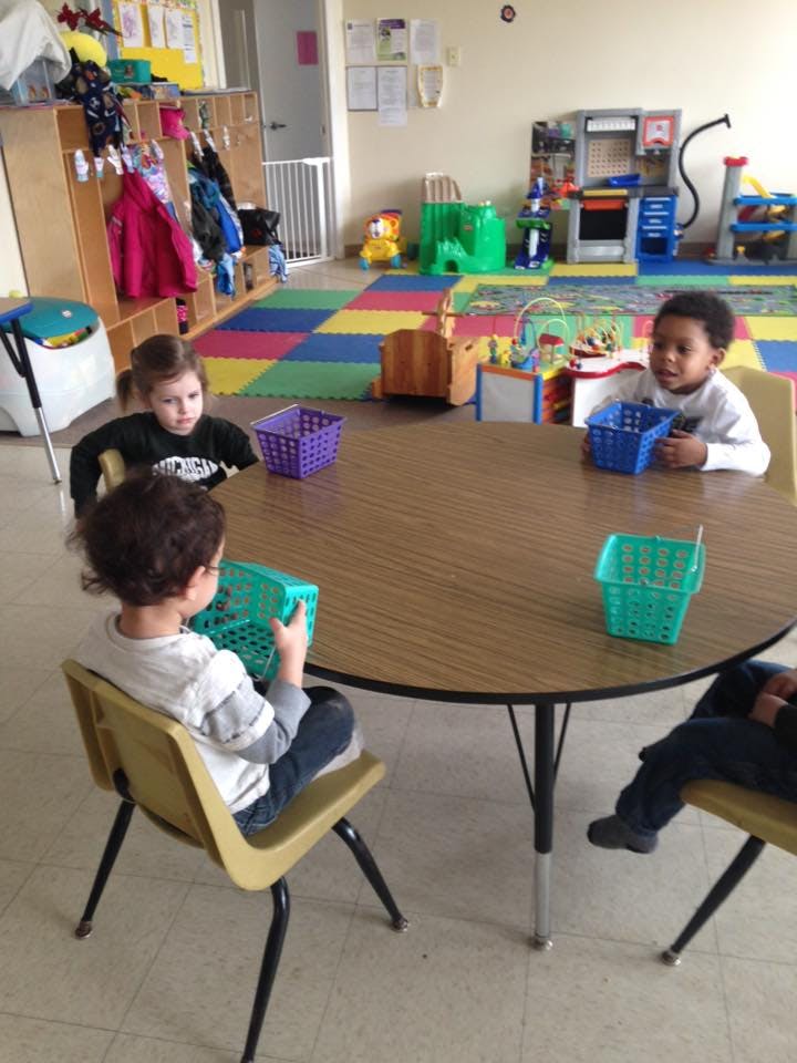 Three children sitting at a round table with small baskets in a classroom