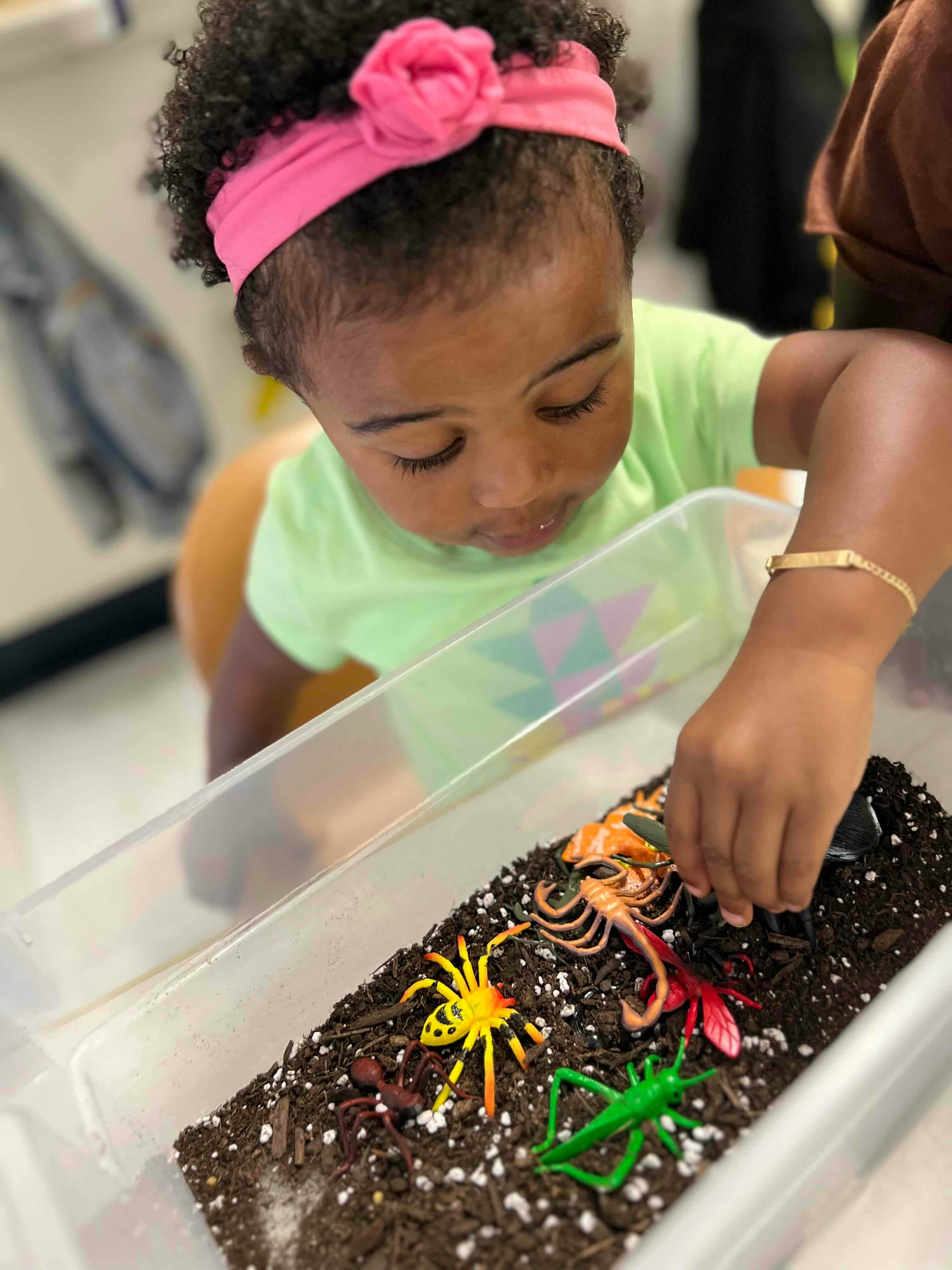 Child looking at and touching toy insects in a container of dirt