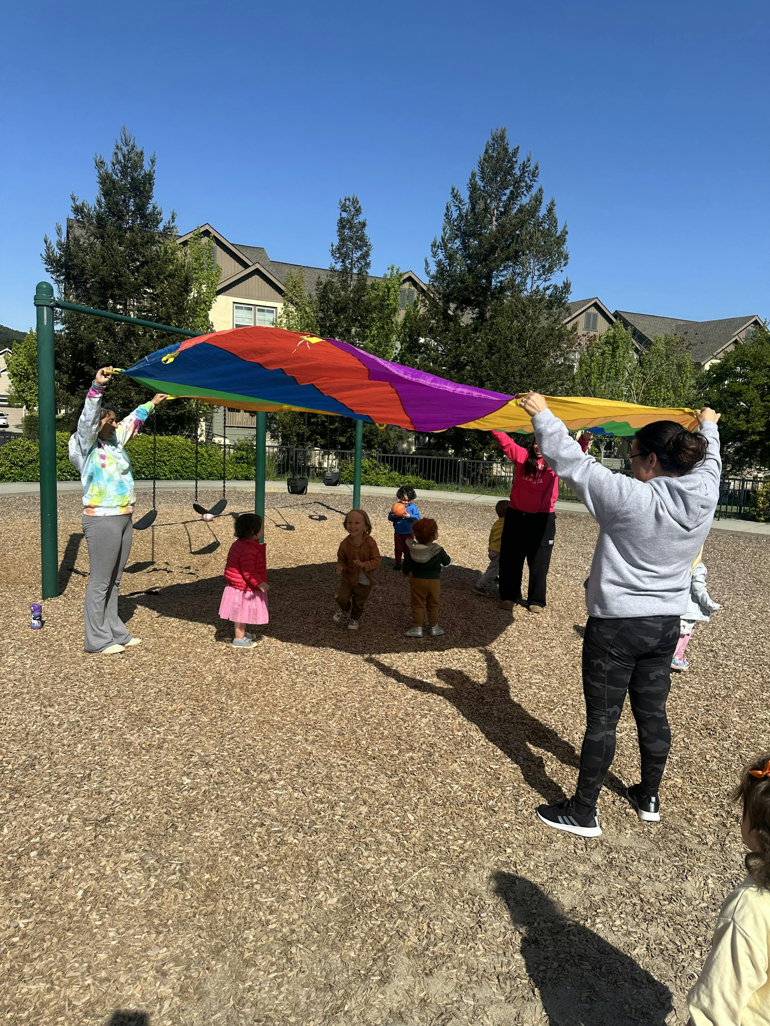 People and children playing with a colorful parachute on a playground