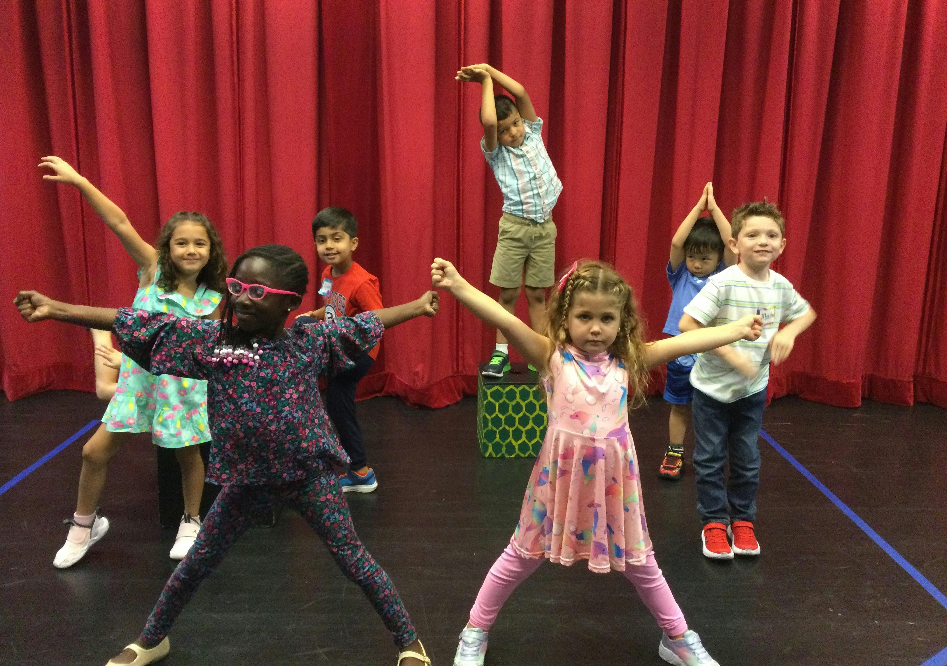 Group of children standing on a stage with red curtains performing poses