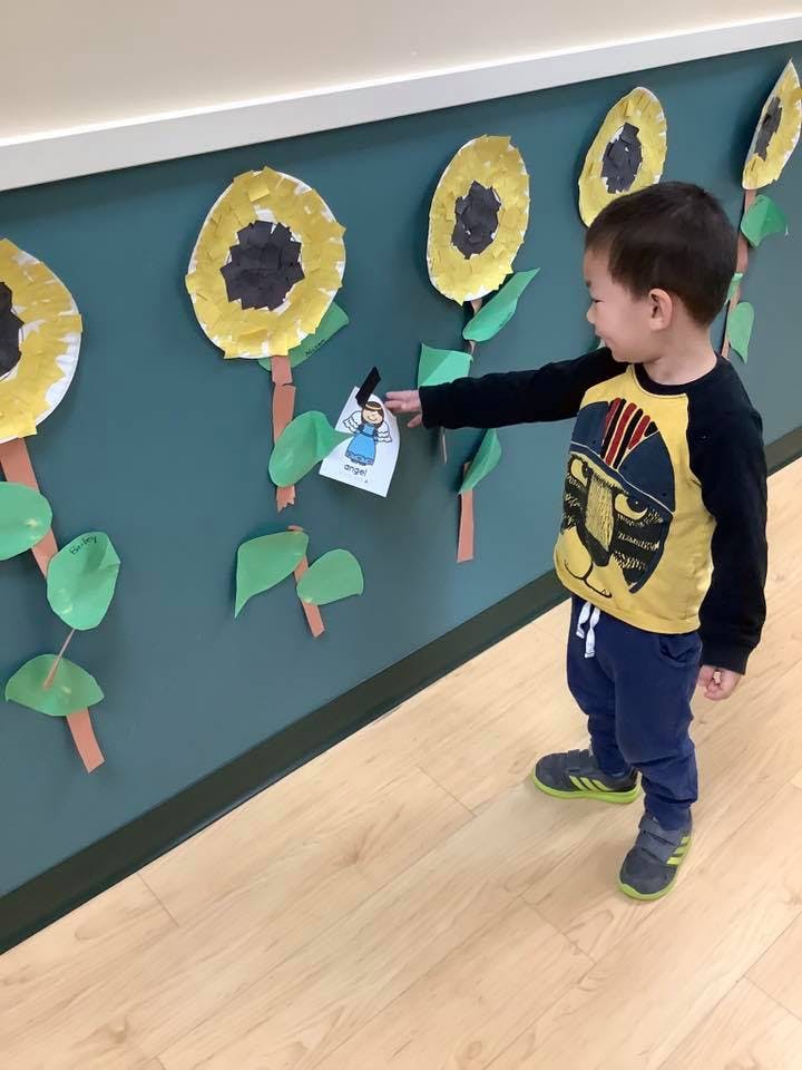 Child interacting with a paper cutout on a wall decorated with sunflowers