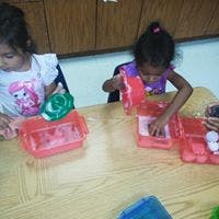 Two children playing with red containers at a table