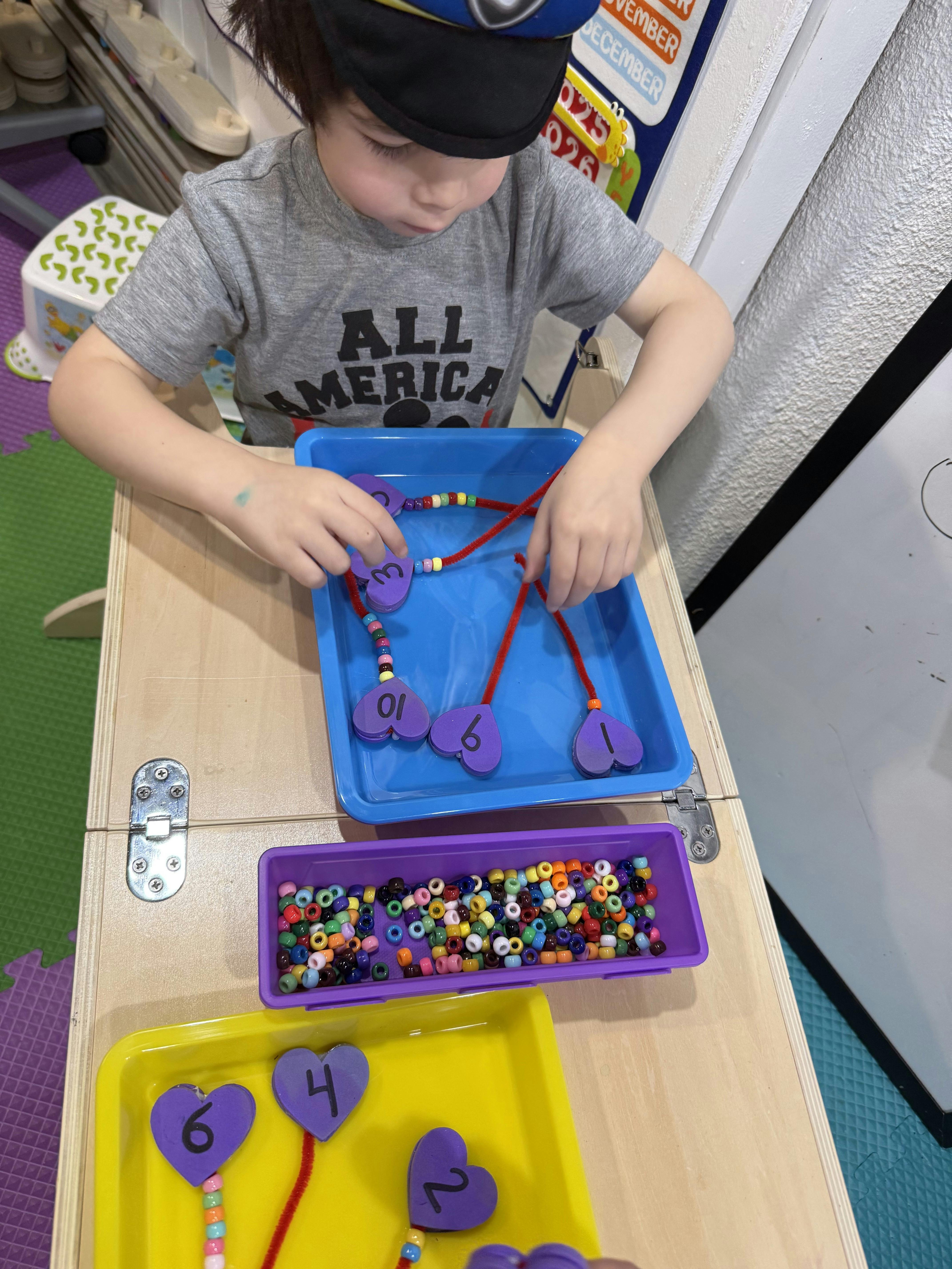 Child threading beads onto pipe cleaners with numbered heart shapes