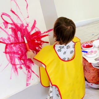 Child in smock painting on a wall