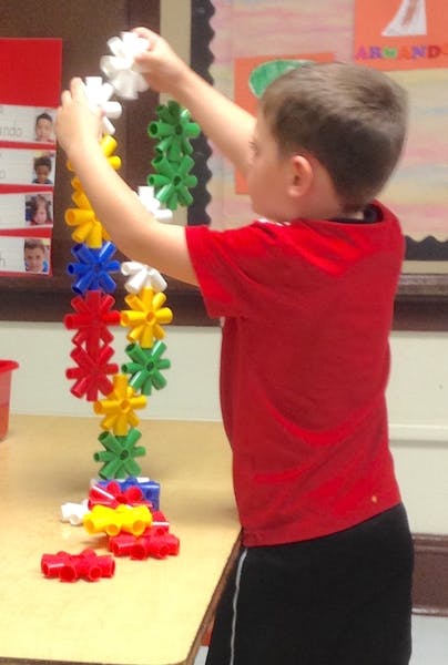 Child building a tall structure with colorful interlocking plastic pieces