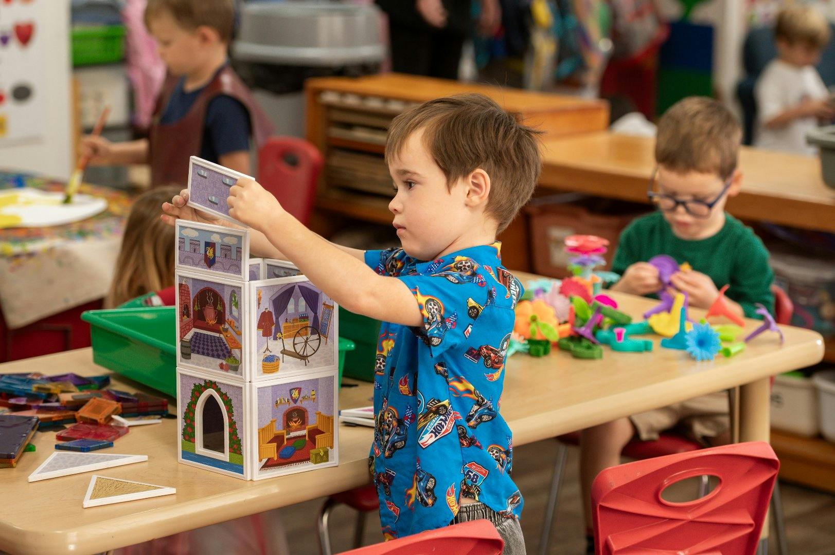 Child building a toy tower at a table in a classroom