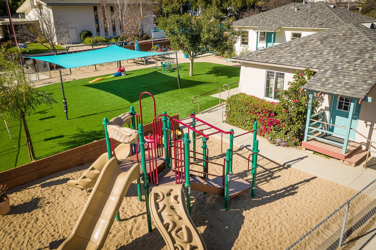 Playground with slides, climbing structure, sand, and artificial turf with shade